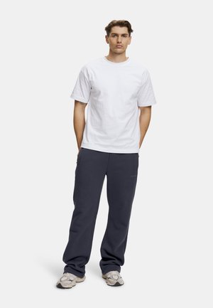 Hvid bomulds t-shirt kombineret med navy sweatpants, der har lommer og logo detaljer. Båret med grå og beige sneakers. Simpelt design.