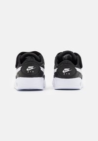 Mustat ja valkoiset Nike Air -tennarit, joissa on tekstuuripinta, sileät nahkaosat, brändätty kanta ja uurrettu valkoinen pohja.
