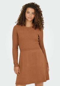 Rjava pletena obleka s rebrastim vzorcem na telu, dolgimi rokavi in razširjenim krilom. Preprosta okrogla izrezana ovratnica, obleka srednje dolžine.