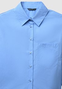Himmelblaues Hemd mit Knöpfen, aus glattem Stoff, mit spitzem Kragen, einer Brusttasche und sechs hellen Knöpfen auf der Vorderseite.