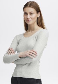 Lys grå langermet topp med ribbestruktur og rund halslinning. Stoffet ser mykt og tettsittende ut, kombinert med mørke denimbukser.