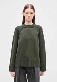 Tume-roheline liistudega kaeluse, varruka ja äärega mahukas kampsun. Valmistatud tekstuurse kudumiga kangast. Pika varrukaga, lõdva lõikega.