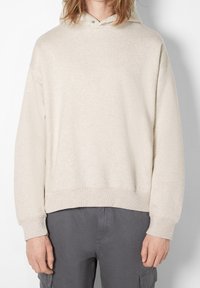 Beige huvtröja i mjukt tyg, med avslappnad passform, ribbad mudd och nederkant. Minimalistisk design utan synliga mönster eller accenter.