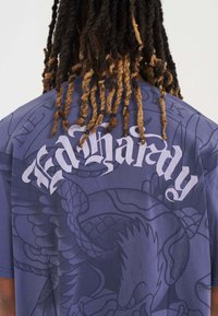 Blå grafisk T-shirt med stor hvid "Ed Hardy" tekst og intrikate design af en drage. Blødt stof med en afslappet pasform.