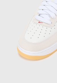 Nike superge z belim usnjem, svetlim sivim svilenimi dodatki, perforiranim prstnim delom, belimi vezalkami in teksturiranim gumijastim podplatom.