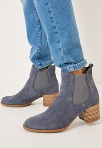 Grå mocka anklarstövlar med elastiska sidopaneler och en strukturerad, staplad klack. Kombinerat med blå denimjeans med uppvikt kant.