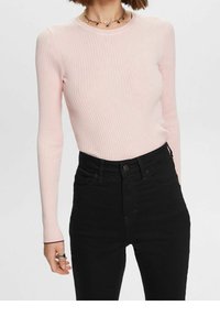 Haut côtelé à manches longues rose clair, associé à un jean noir taille haute, présentant une coupe ajustée et un col rond.