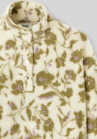 Pull en polaire avec un imprimé floral vert et violet sur un fond crème. Il dispose d'un col à bouton et d'une texture douce.