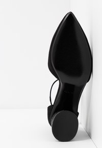 Chaussure noire à bout pointu avec dessus en daim texturé et semelle synthétique brillante. Caractérisée par un talon élancé et un design épuré.