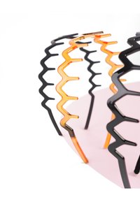 Decoratief object met een zigzagpatroon in zwart en oranje, gemaakt van plastic, met een roze basis. Het heeft een open ontwerp en variërende hoogtes.