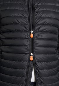 Gilet imbottito nero con zip verticale dotata di linguette arancioni, texture trapuntata e materiale leggero. Il design è senza colletto e aderente.