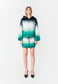Conjunto de chaqueta con capucha y falda mini en una mezcla ombré de negro, verde y blanco. Presenta accesorios de metal, puños elásticos y un diseño deportivo.