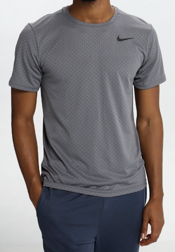 T-shirt de sport gris avec une texture géométrique subtile et un logo Nike noir en haut à gauche. Manches courtes, design col rond.