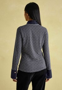 Navy-Bluse mit geometrischem Muster, kontrastierendem Kragen und Manschetten sowie einer glatten Textur. Rückansicht angezeigt.