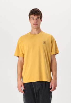 T-shirt di cotone gialla con collo a giro e maniche corte, caratterizzata da una patch quadrata sul petto. Vestibilità casual, texture morbida.