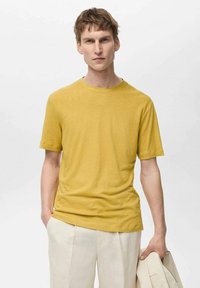 Kortærmet gul T-shirt i et blødt, let materiale med rund halsudskæring, parret med lyse bukser. Simpelt, afslappet design.