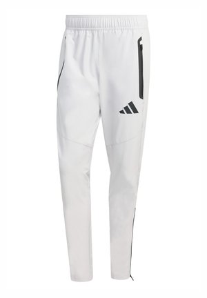 Pantalones deportivos blancos con cinturilla elástica, bolsillos laterales con cremallera y detalles en negro. Presentan el logo de Adidas en negro en la pierna izquierda.