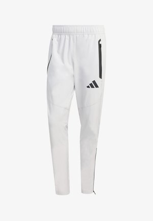 Pantalones deportivos blancos con cinturilla elástica, bolsillos laterales con cremallera y detalles en negro. Presentan el logo de Adidas en negro en la pierna izquierda.