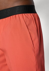 Herren Shorts in einem Korallenfarbton, aus leichtem Stoff gefertigt. Sie verfügen über einen elastischen schwarzen Bund mit dem Aufdruck 'ENDLESS' und seitlichen Taschen.
