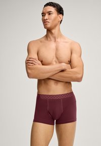 Viininpunaiset boxerit, joissa on teksturoitu vyötärönauha, tiukka istuvuus ja saumaton muotoilu, mallin päällä, jolla kädet ristissä.