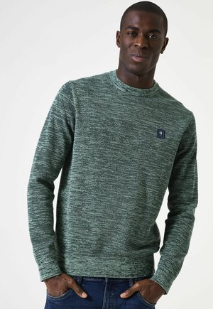 Groene gebreide trui met lange mouwen, ronde halslijn en een klein blauw logo-opgenaaid op de borst. Draag het met blauwe spijkerbroek.