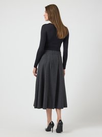 Top negro de manga larga combinado con una falda gris de longitud hasta la rodilla, plisada y hecha de un tejido texturizado, llevada con zapatos de tacón alto negros.