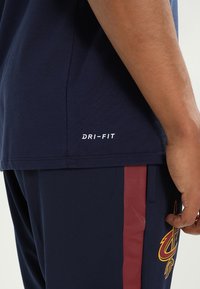 Marineblå DRI-FIT t-shirt med korte ærmer og sideslids, glat tekstur; kombineret med marineblå shorts med en mørkerød stribe og logodetalje.