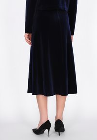 Navy fluwelen midi-rok met een uitlopende zoom, een gladde textuur en onzichtbare naden; gecombineerd met zwarte hoge hakken.