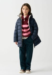 Námornícka pufovaná bunda s kapucňou cez prúžkovaný bordový a ružový sveter, v kombinácii s tyrkysovými kordovým nohavicami a hnedými teniskami.