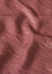 Tissu doux et froissé de couleur rose poudrée avec une texture subtile et des reflets de lumière sur toute la surface.