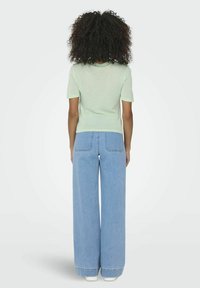 Top verde menta a maniche corte abbinato a jeans a gamba larga blu chiaro. Entrambi gli articoli presentano un fit casual e rilassato con un design semplice.