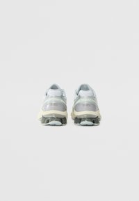 White and grey athletic shoes with a textured upper, reflective accents, and a distinct cushioned sole; rear view shows design details.