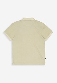 Poloshirt mit kurzen Ärmeln aus weichem, hellem beigen Stoff, mit einem Kragen und einem schlichten Design. Ein kleines Markenlabel befindet sich unten links.