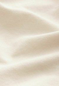 Tissu en coton de couleur écrue avec une texture douce et lisse et de subtils motifs de tissage en diagonale, présenté dans de douces plissures.
