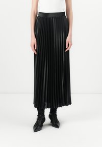 Fekete, plisszézett szoknya fényes anyagból, magas derékkal és floor-length kialakítással, hegyes fekete cipőkkel és fekete zoknikkal párosítva.