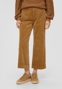 Bruine corduroy wijde broek met opgerolde pijpen, gecombineerd met tan sneakers. De stof heeft een gestructureerde afwerking.