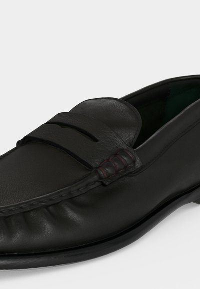 Mocassin en cuir noir à enfiler avec un bout mocassin cousu et une bride décorative sur le dessus.