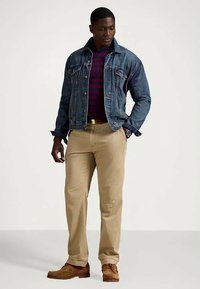 Casaco de ganga, camisa às riscas em vermelho escuro e azul-marinho, calças bege claro, sapatos castanhos com atacadores; o conjunto apresenta um estilo casual e ajustado.