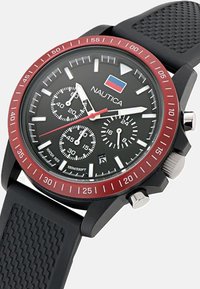 "Nautica" chronografas su juodu guminio dirželiu. Apvalus juodas ciferblatas, raudona rėmelis, sidabriniai akcentai ir trys laikmačių subdalykiai. Atsparus vandeniui.