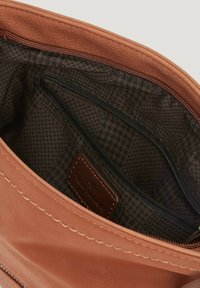 Interior de bolsa de cuero marrón con un patrón de houndstooth oscuro. Presenta un bolsillo con cremallera y una etiqueta de cuero. Se pueden ver los bordes cosidos.