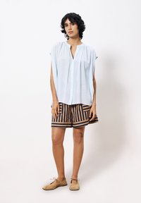Lichtblauwe kortom mouwende blouse, gecombineerd met beige en marineblauwe gestreepte shorts. Zachte textuur, losse pasvorm en minimalistisch ontwerp.