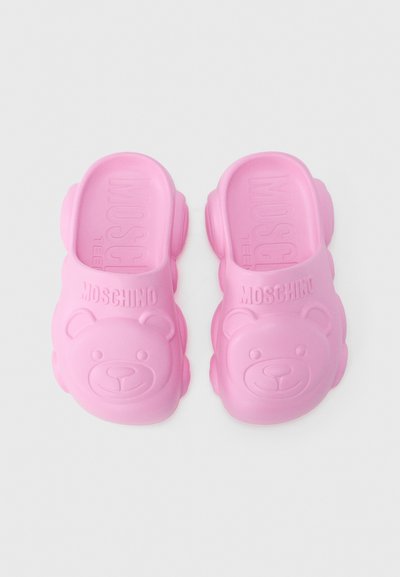 Sabots en caoutchouc roses avec un motif de visage d'ours à l'avant, portant l'inscription "Moschino" en relief sur le côté supérieur et des bords arrondis et texturés.