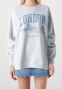 Sudadera gris con gráfica en azul de "LONDRES" y el horizonte, con cuello redondo y mangas largas, combinada con una falda de mezclilla.
