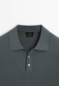Polo shirt grigio a costine con colletto, caratterizzato da tre bottoni argentati e un'etichetta di marca all'interno del collo. Tessuto liscio e design aderente.