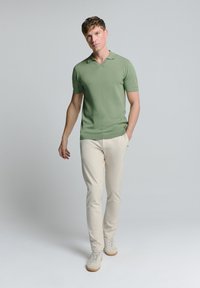 Lichtgroene polo met korte mouwen van een gladde stof, gecombineerd met crèmekleurige slim-fit broek en beige sneakers.