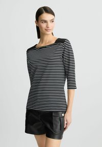 Zwart-wit gestreepte shirt met een vierkante halslijn en decoratieve studs. Met driekwartmouwen en een getailleerd ontwerp.