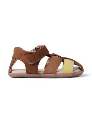 Sandalia de cuero marrón con lados abiertos, cierre de velcro y acento amarillo en la parte delantera. Suela plana con textura suave.