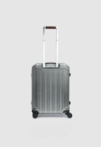 Silberner Hartschalen-Kabinenkoffer mit vertikalen Rillen, ausziehbarem Griff und vier Rollen für Mobilität. Verfügt über einen braunen Griffakzent.