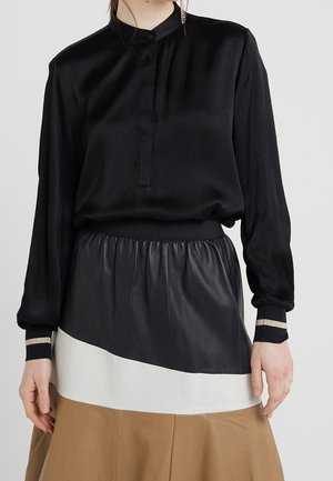 Black blouse with a buttoned collar and long sleeves, paired with a pleated black leather and beige skirt. The blouse has a soft, shiny texture.