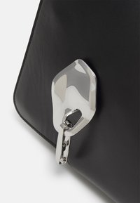 Geantă din piele neagră, cu un accent de metal argintiu lucios, având o formă geometrică unică, atașată printr-o legătură metalică. Textură netedă.